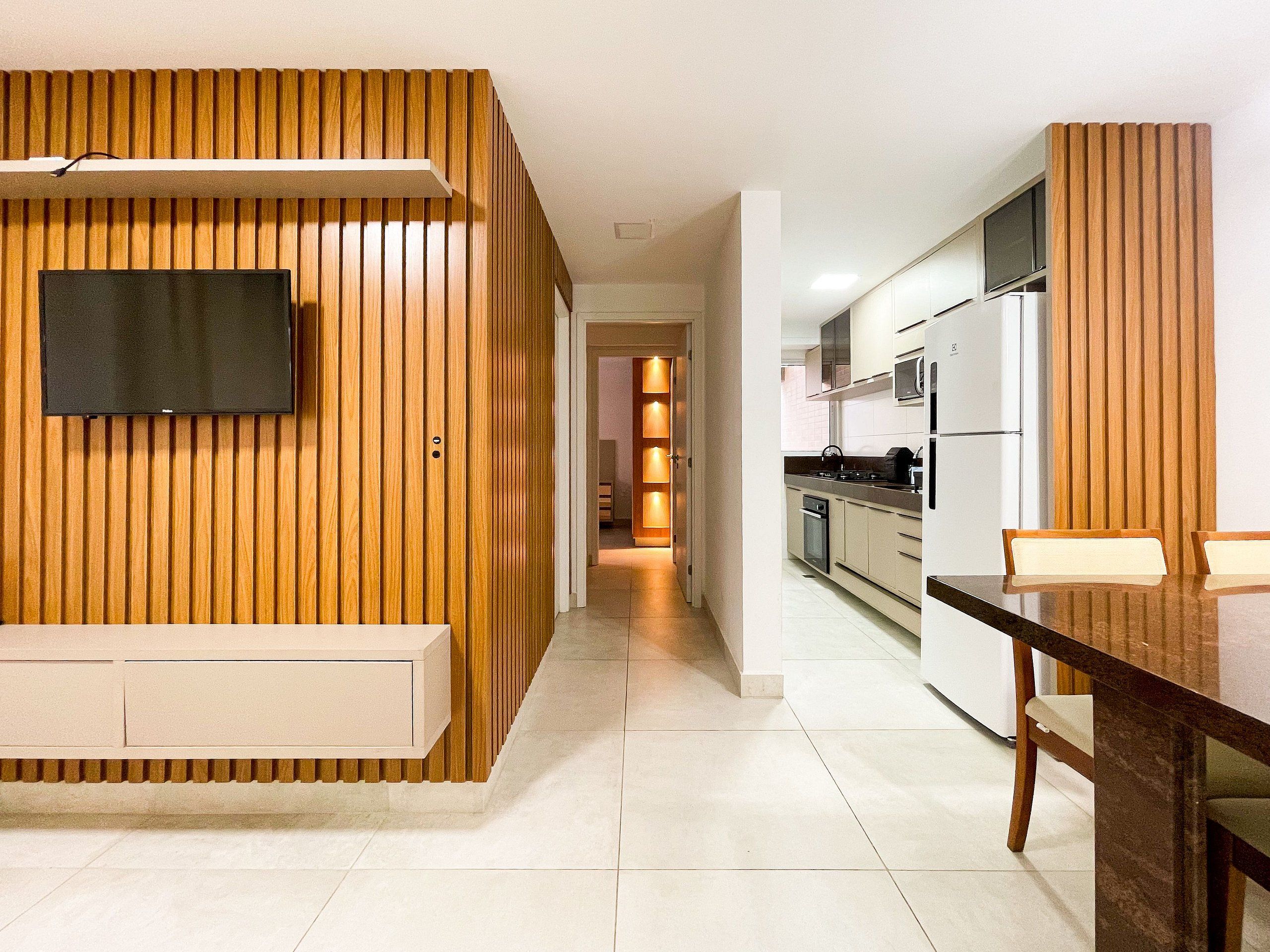 A modern kitchen with wooden paneling, a dining area with a table and chairs, and a TV mounted on the wall.