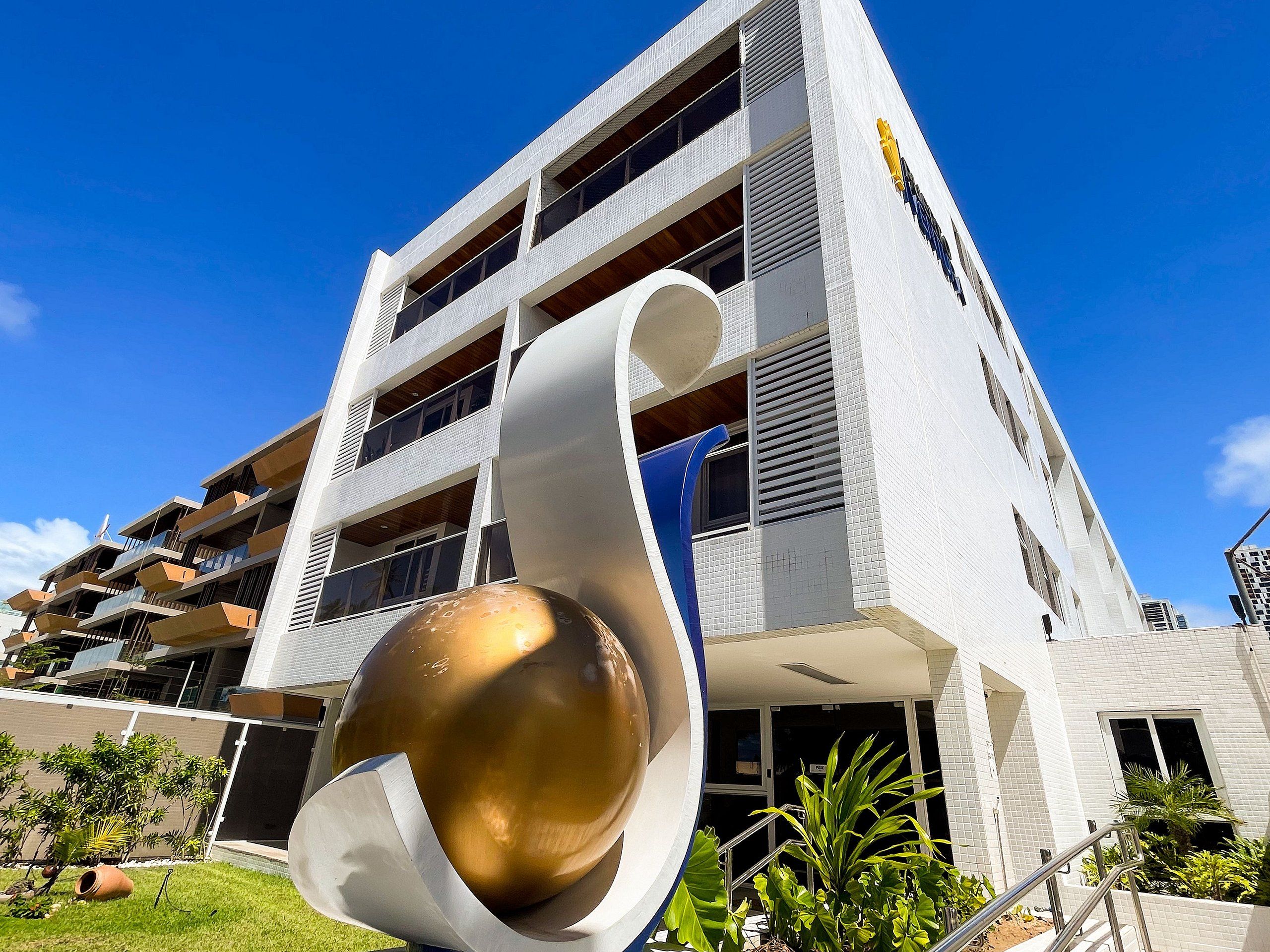 A modern building with a unique architectural design, featuring a large golden spherical sculpture in the foreground.