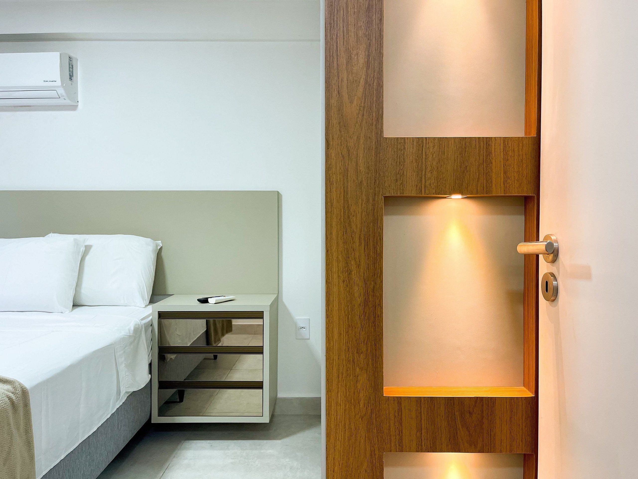 Habitació d'hotel amb llit, taula de nit i porta de fusta amb mirall.