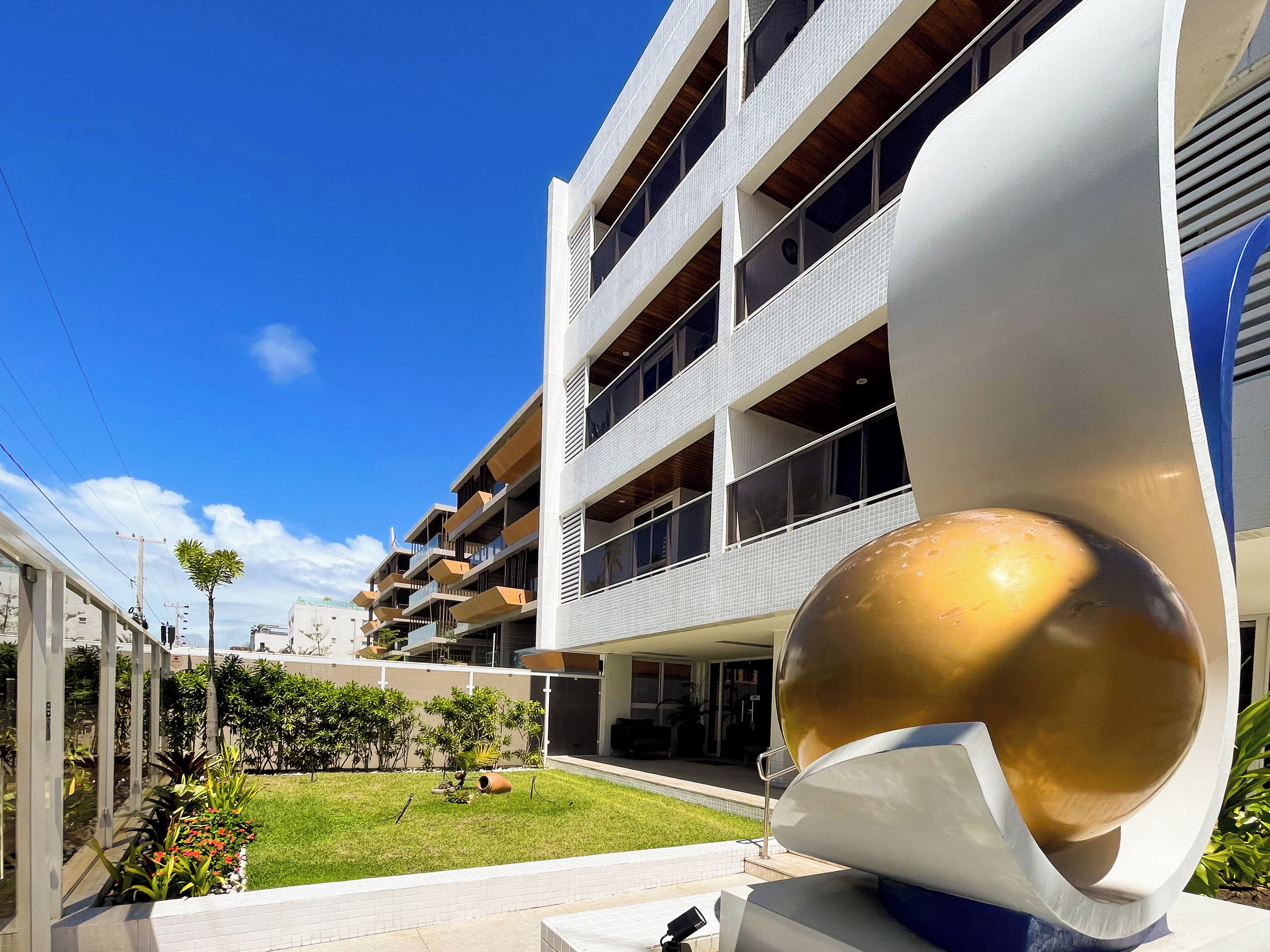A modern building with multiple balconies, a well-maintained lawn, and a large spherical sculpture.