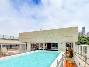 Piscina no terraço com um edifício moderno ao fundo.