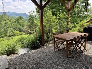 An outdoor wooden table and chairs set on a gravel surface, surrounded by greenery and a view of a mountainous landscape. - Mountain Peace 25 Min from Downtown Asheville (Barnardsville)