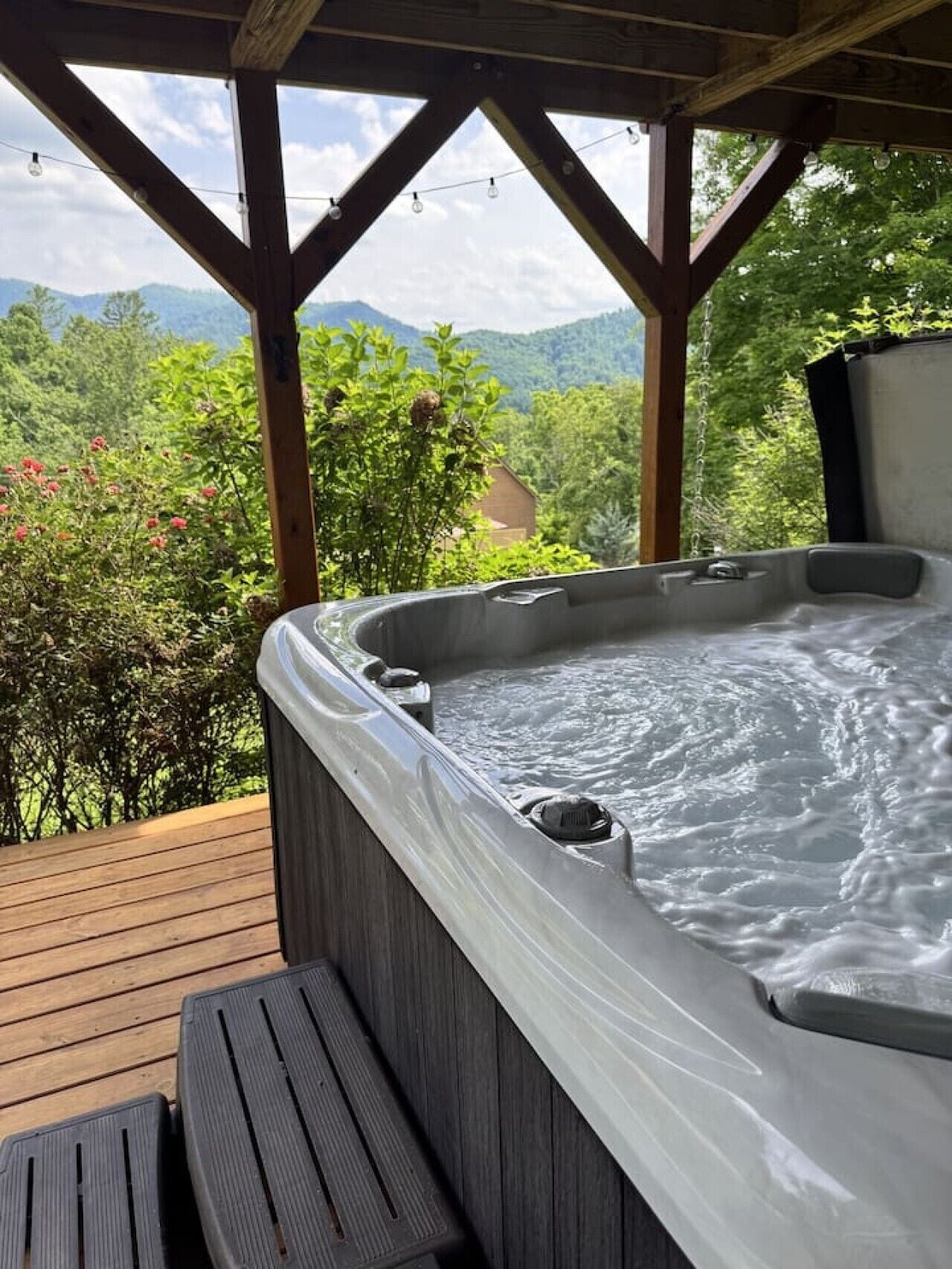 A hot tub on a wooden deck with a view of mountains and trees.