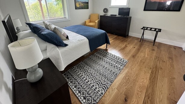 A bedroom with a bed, bedside table, lamp, dresser, chair, and artwork on the walls. - Mountain Peace 25 Min from Downtown Asheville (Barnardsville)
