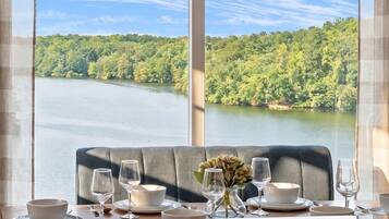 A dining table set with glasses and bowls, a vase with flowers, and a view of a lake surrounded by trees.