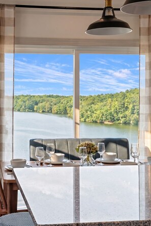 Una mesa de comedor dispuesta con vasos y cuencos, un jarrón con flores y vistas a un lago rodeado de árboles.