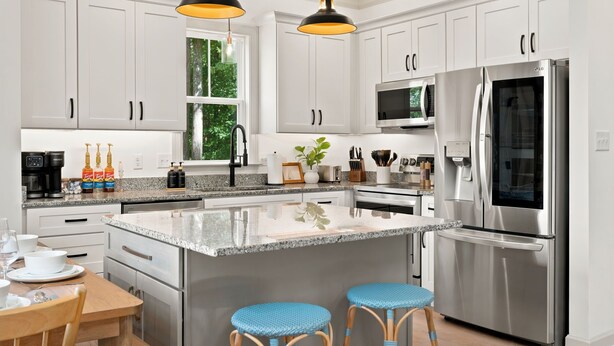 Una cocina moderna con electrodomésticos de acero inoxidable, armarios blancos y encimera de granito.