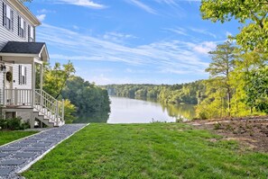 A house with a porch, a stone pathway, and a view of a lake surrounded by trees.