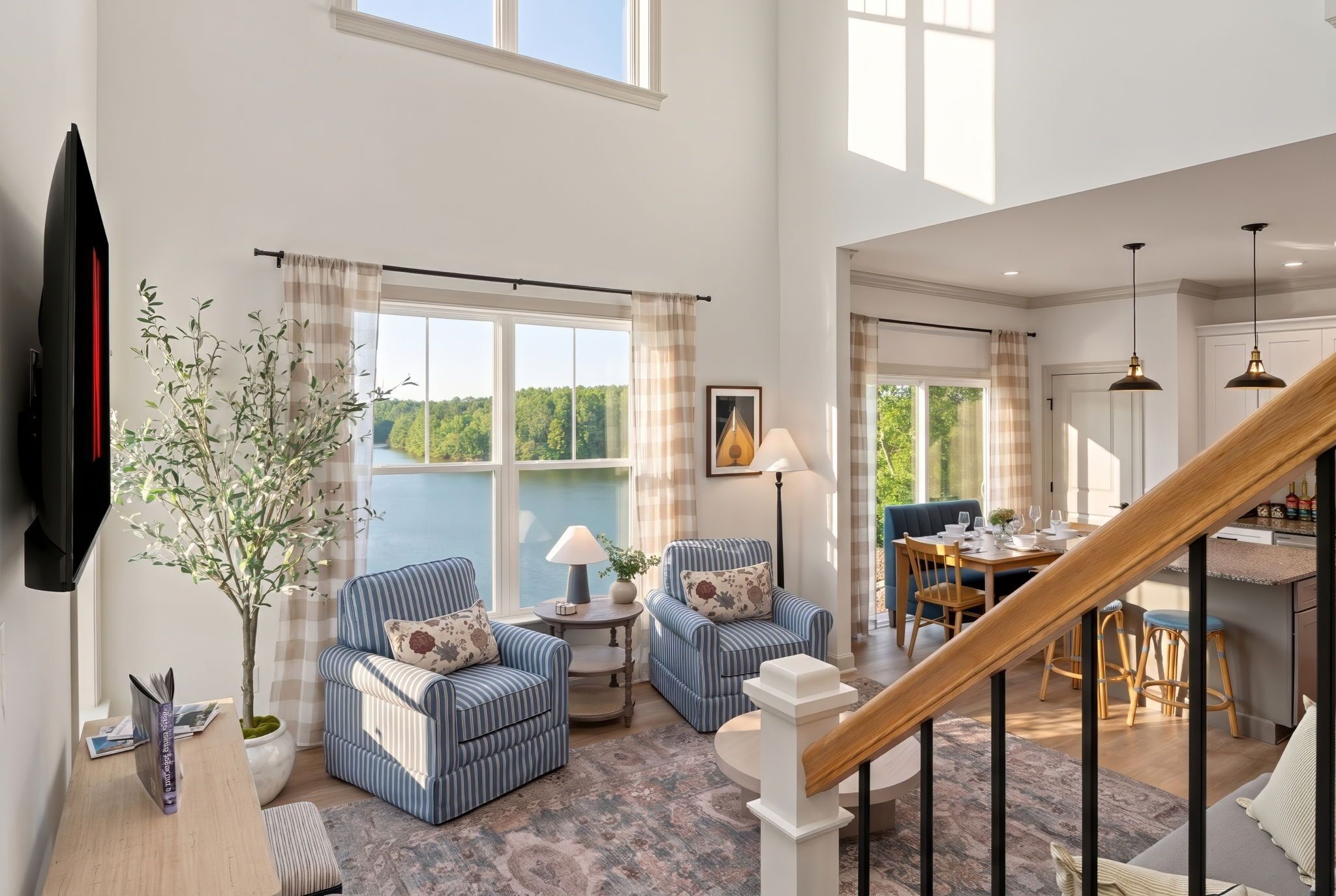 A spacious living area with a view of a lake, a dining area, and a staircase.
