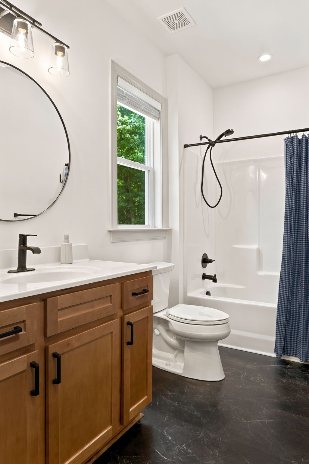 A bathroom with a white sink, wooden cabinets, a toilet, a shower with a glass door, and a window with a view of trees.