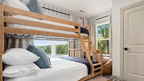 Una cama individual superpuesta con escalera, una ventana con vista a árboles y una puerta.
