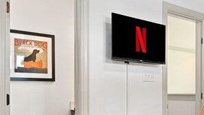 Una habitación con puerta, un cuadro enmarcado, un televisor montado y suelo cubierto de alfombra.