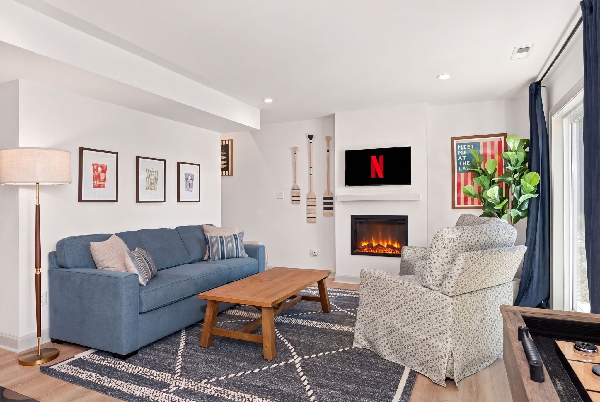 A modern living room with a blue sofa, a wooden coffee table, a patterned armchair, a fireplace, and a mounted TV.