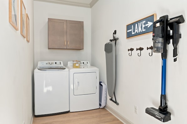 A laundry room with two washing machines, a drying rack, and a vacuum cleaner.