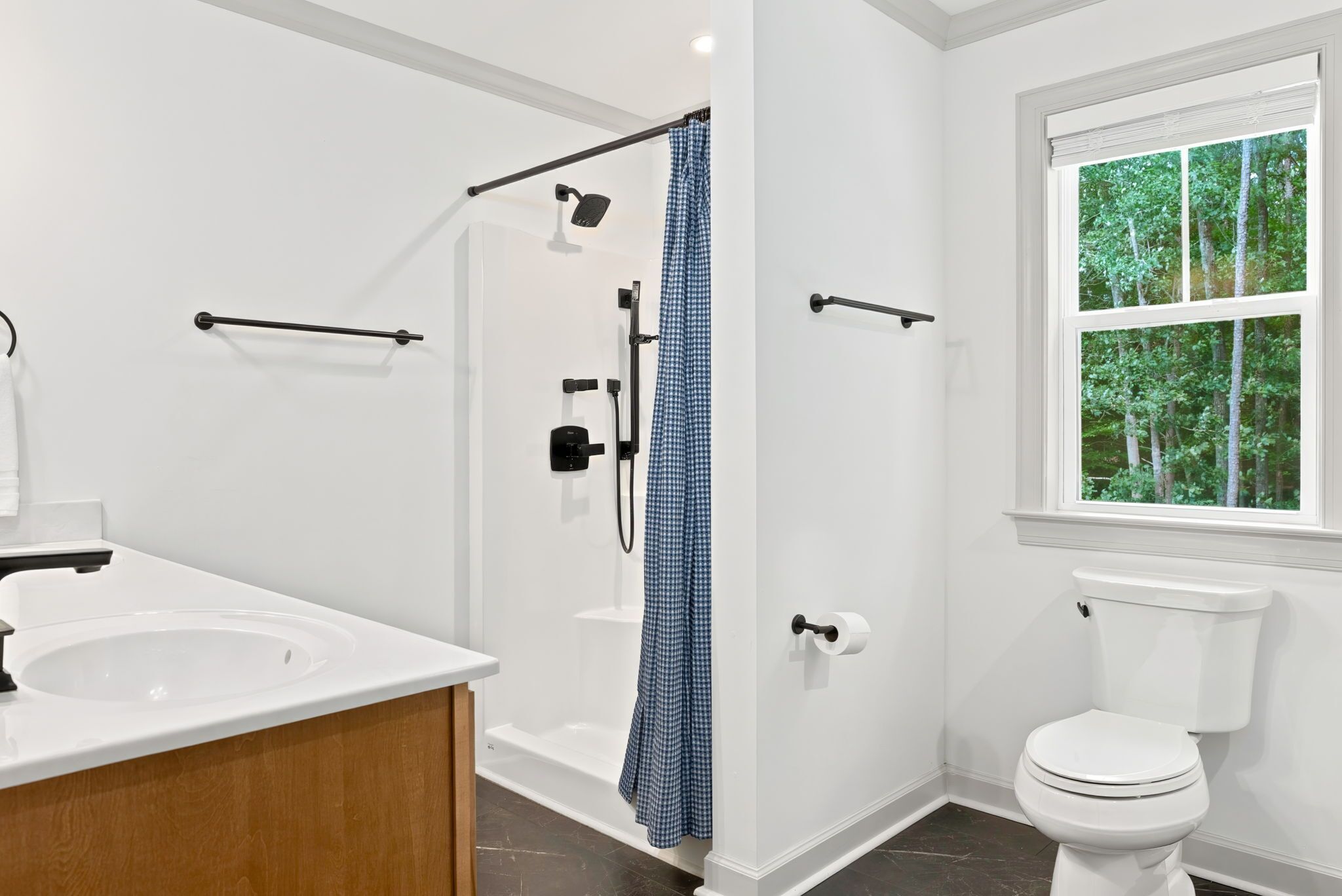 Une salle de bain moderne équipée d’une douche, de toilettes et d’une fenêtre donnant sur la verdure.