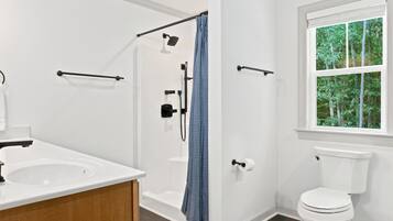 Une salle de bain moderne équipée d’une douche, de toilettes et d’une fenêtre donnant sur la verdure.