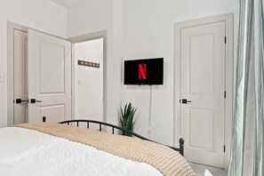 Un dormitorio con una cama, un televisor montado en la pared y una planta.
