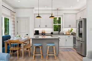 A modern kitchen with white cabinetry, a central island with stools, a built-in oven, and a refrigerator. - NEW Williamsburg, Long Range Lake Views, Hot Tub, Sauna, Fire Pit, Game Room (Lanexa)