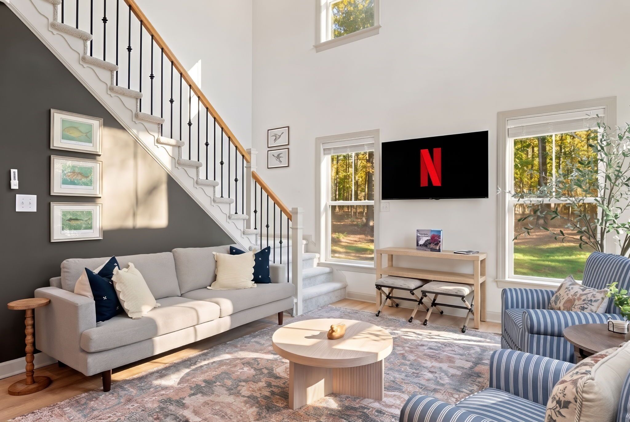 Sala de estar con una escalera, un sofá, una mesa de centro, un televisor y vistas al exterior.