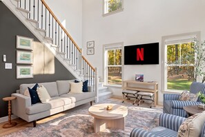 Sala de estar con una escalera, un sofá, una mesa de centro, un televisor y vistas al exterior.