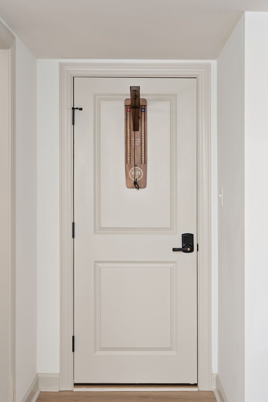 En hvid dør med et traditionelt design, et trægreb og en moderne elektronisk lås.