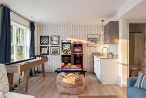 A cozy living room with a pool table, a bean bag, and a kitchen area with a sink and cabinets.