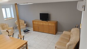 Een woonkamer met een houten kast, een televisie en twee beige fauteuils.