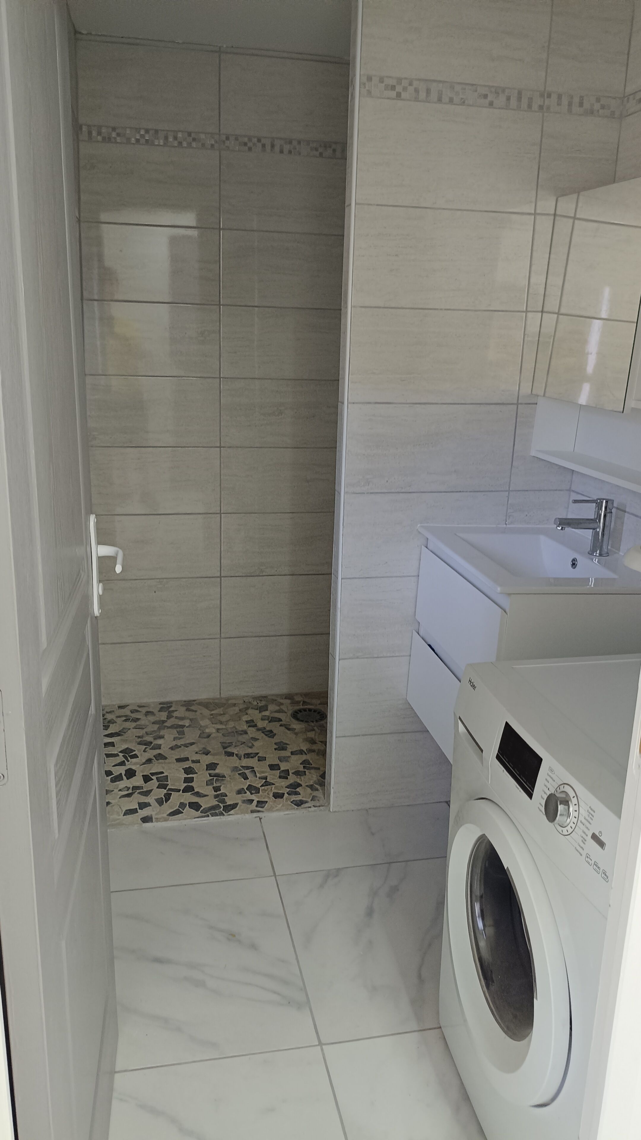 Une petite salle de bain équipée d’un lave-linge, de toilettes et d’un espace douche.
