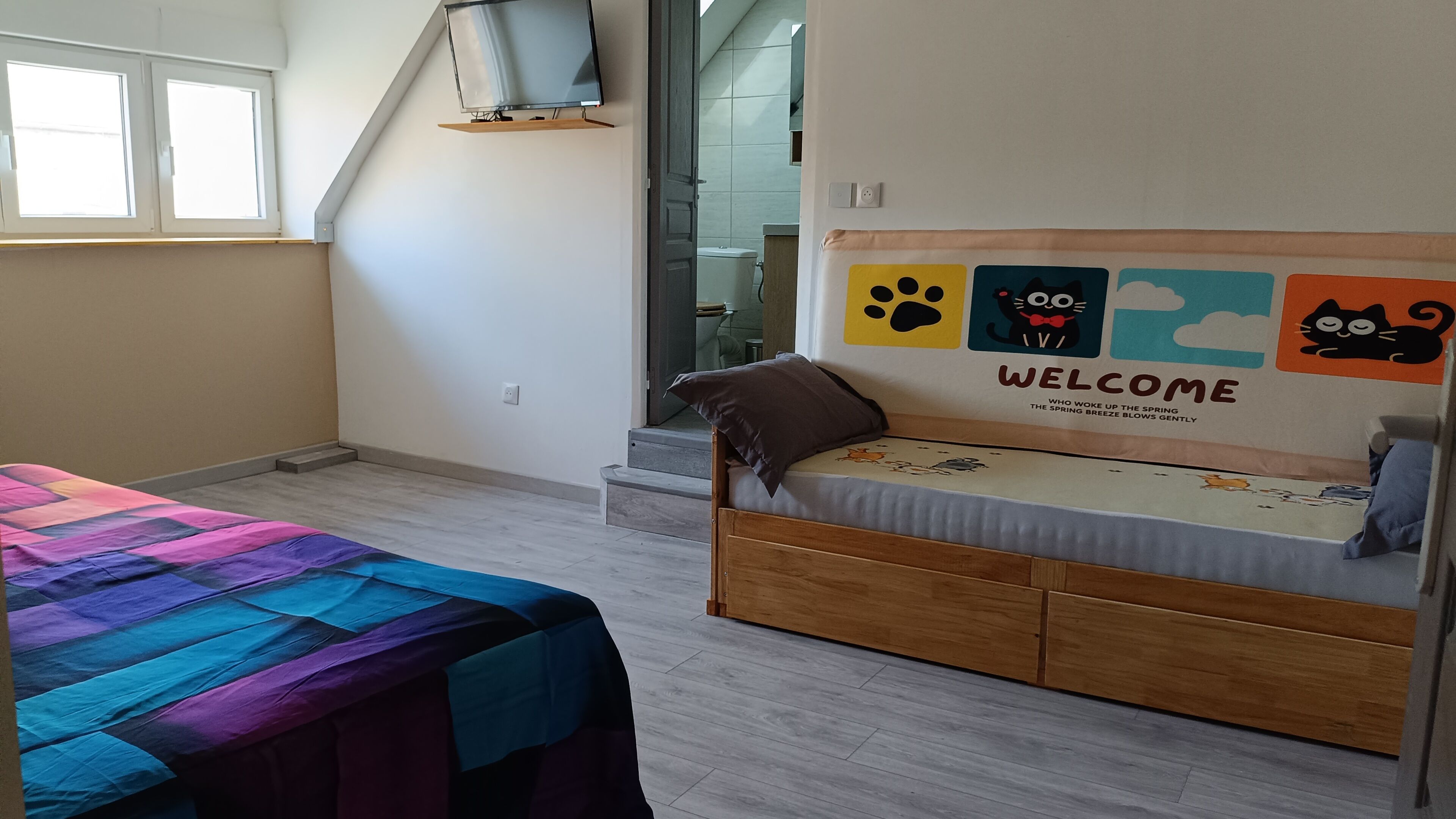 Een kamer met een bed, een raam, een wand met een welkomstbord en een trap die naar een andere kamer leidt.