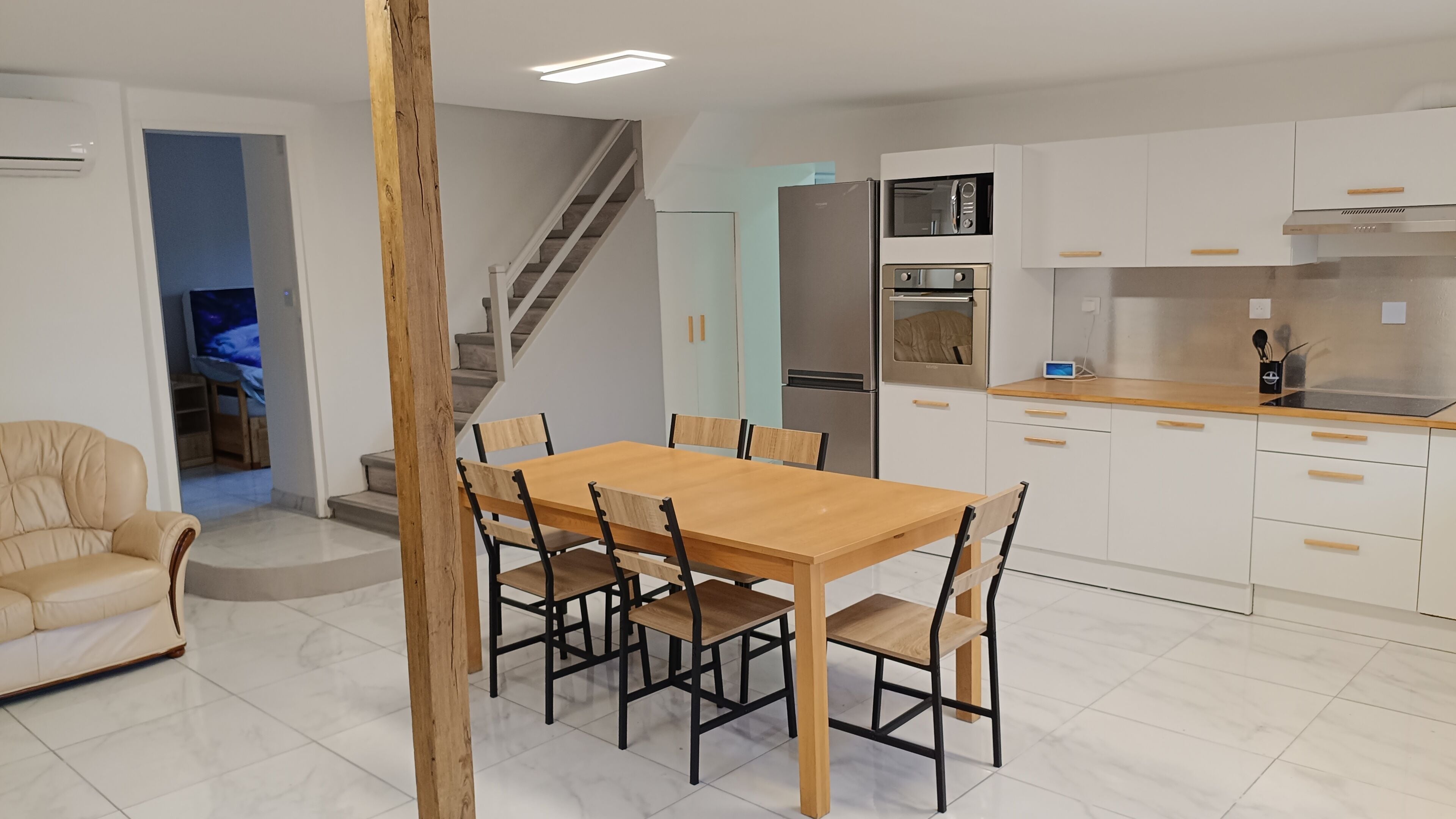 Une cuisine moderne avec des meubles blancs, une table à manger en bois et un four encastré.