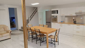 Une cuisine moderne avec des meubles blancs, une table à manger en bois et un four encastré.
