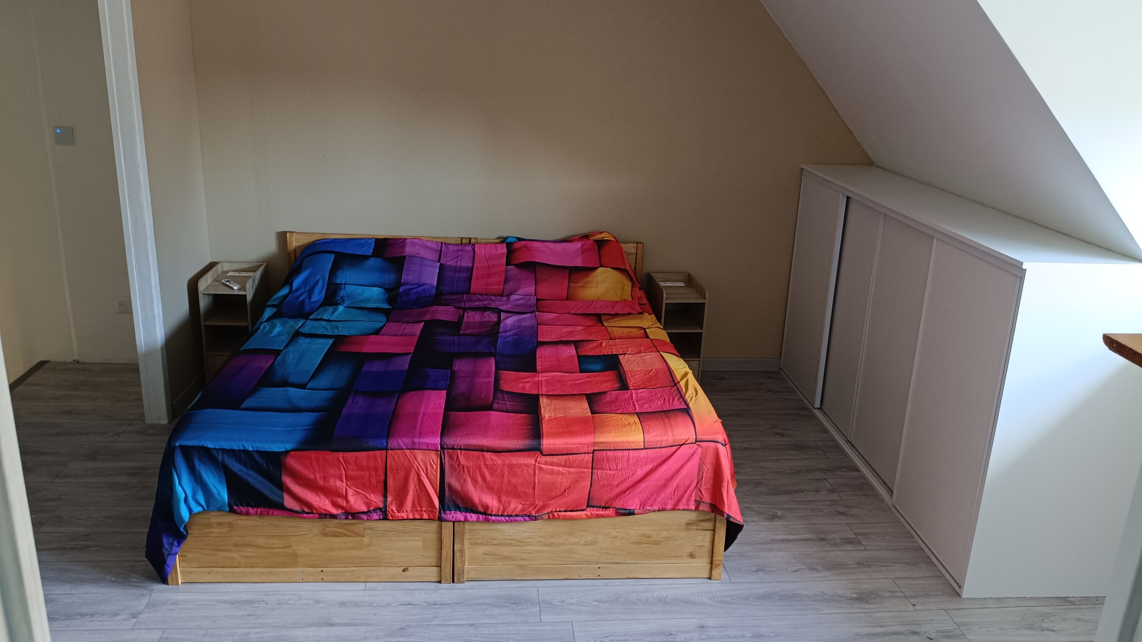 Un dormitorio con cama de madera, colcha colorida y armario blanco.