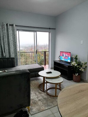 Una sala de estar con sofá, dos mesas redondas, televisor y un balcón con vistas.