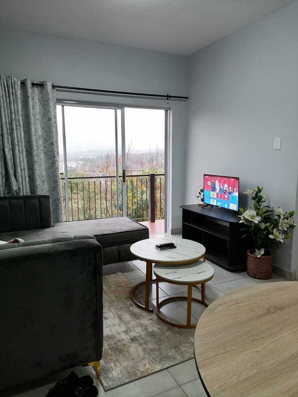 A living room with a sofa, two round tables, a television, and a balcony with a view.