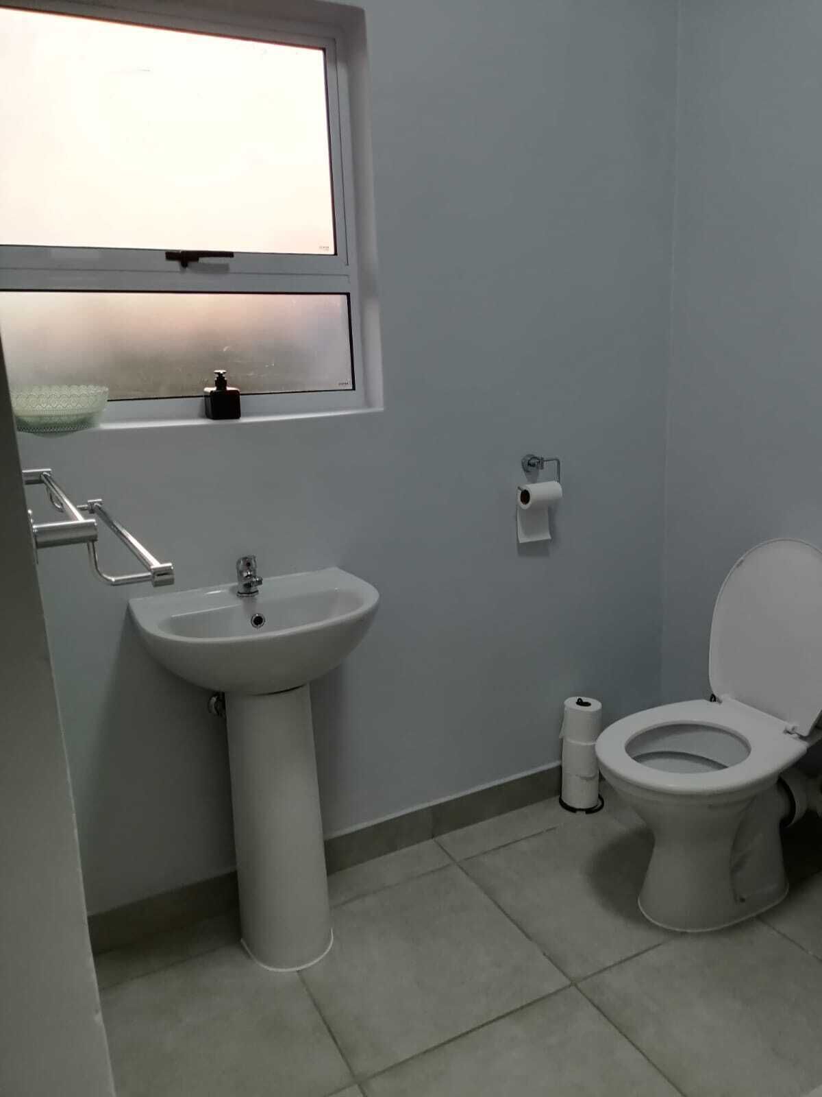 Un baño con lavamanos pedestal, inodoro y ventana sobre el lavamanos.