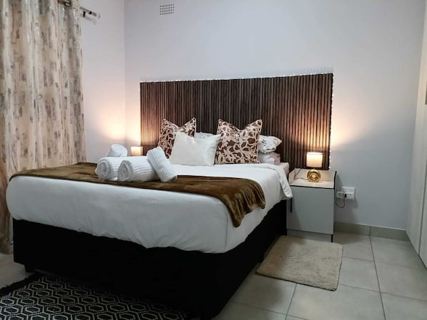 A hotel room with a bed, pillows, a bedside lamp, and a nightstand.