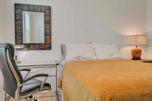 A hotel room with a bed, a desk with a chair, a lamp, and a mirror on the wall. - Contemporary Hideaway • PS4 Console & Games • Fire Pit & Turf (North Las Vegas)