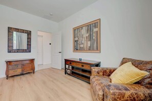 A room with a wooden floor, a vintage-style dresser, a modern sofa with a patterned cover, and a large abstract painting on the wall. - Contemporary Hideaway • PS4 Console & Games • Fire Pit & Turf (North Las Vegas)