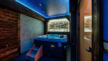 A room with a starry ceiling, a hot tub, and a window with a snowy mountain view.