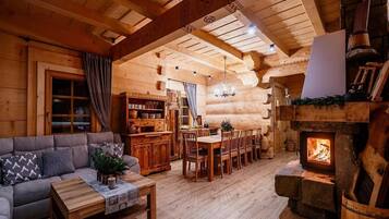 A cozy log cabin interior with a fireplace, wooden furniture, and a dining area.