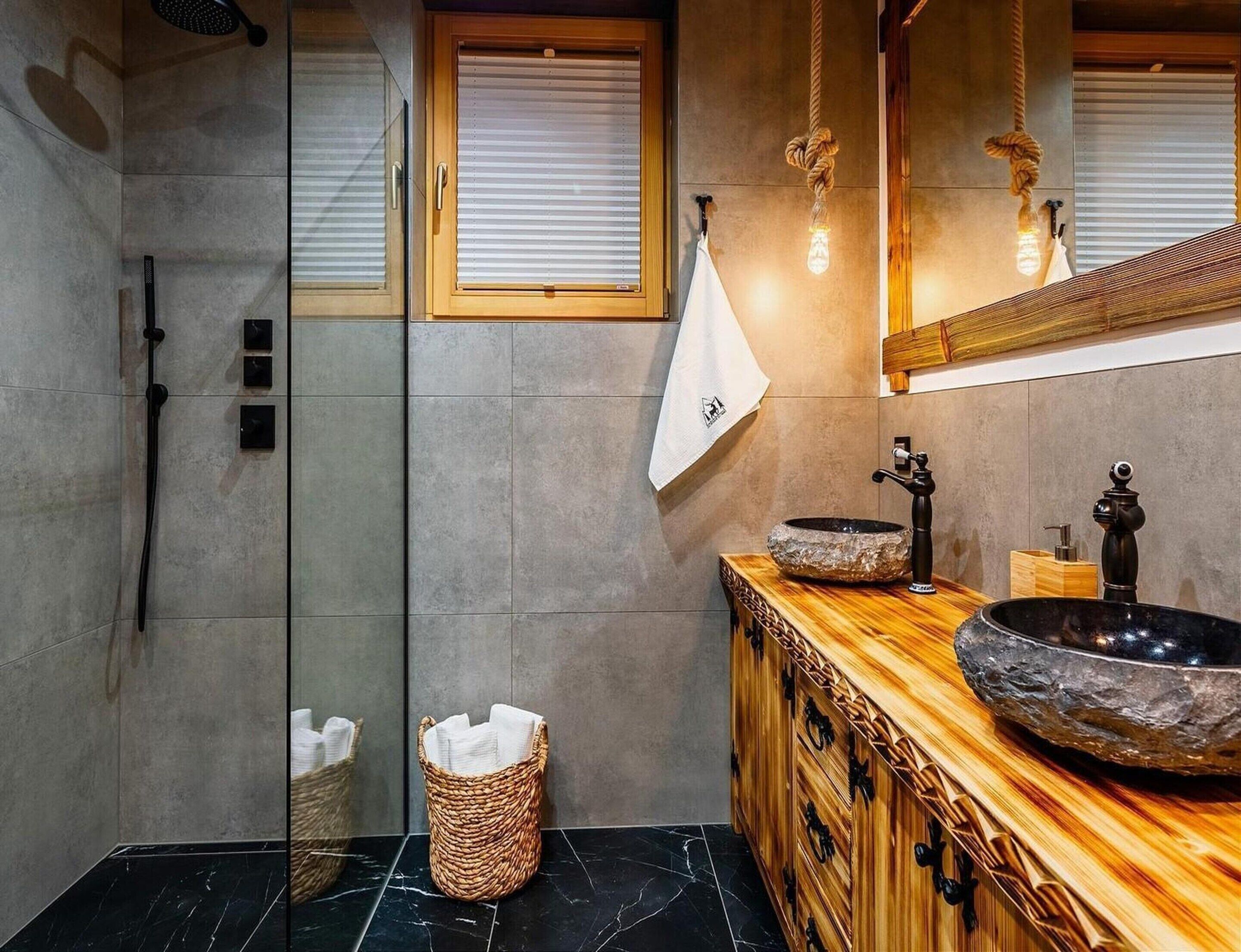 Un baño con ducha envuelta en vidrio, tocador de madera con lavabo de piedra y lámpara colgante.