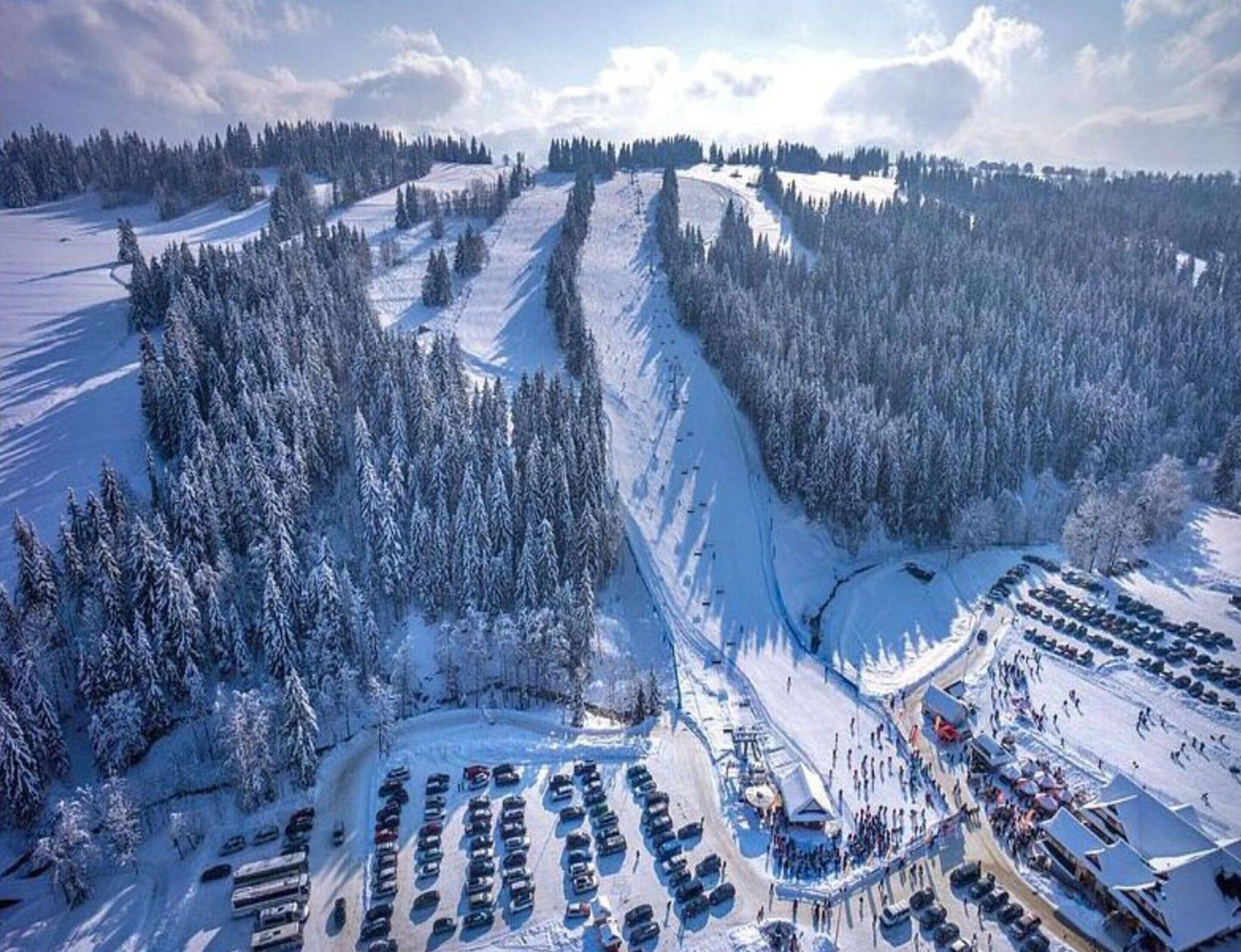 A snow-covered parking lot with rows of cars and a building with a sloped roof.
