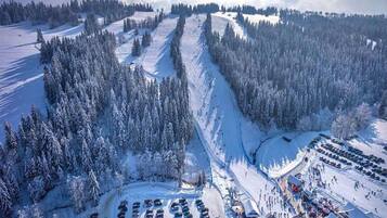A snow-covered parking lot with rows of cars and a building with a sloped roof.