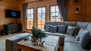 A cozy log cabin interior with a sofa, a coffee table, a television, and a window with curtains. - A Large Mountain-style House With a spa Area (Poronin)