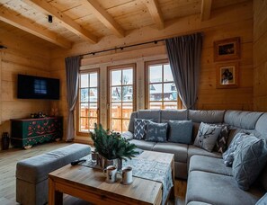 Ein gemütliches Blockhaus-Interieur mit einer Couch, einem Couchtisch, einem Fernseher und einem Fenster mit Vorhängen.