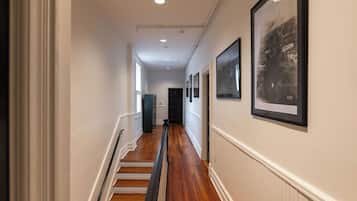 A hallway with wooden flooring, white walls, and framed pictures on the right.