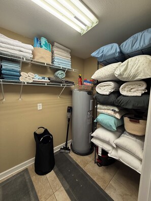 Une pièce de rangement avec des étagères remplies de linge plié, un aspirateur et un grand chauffe-eau.