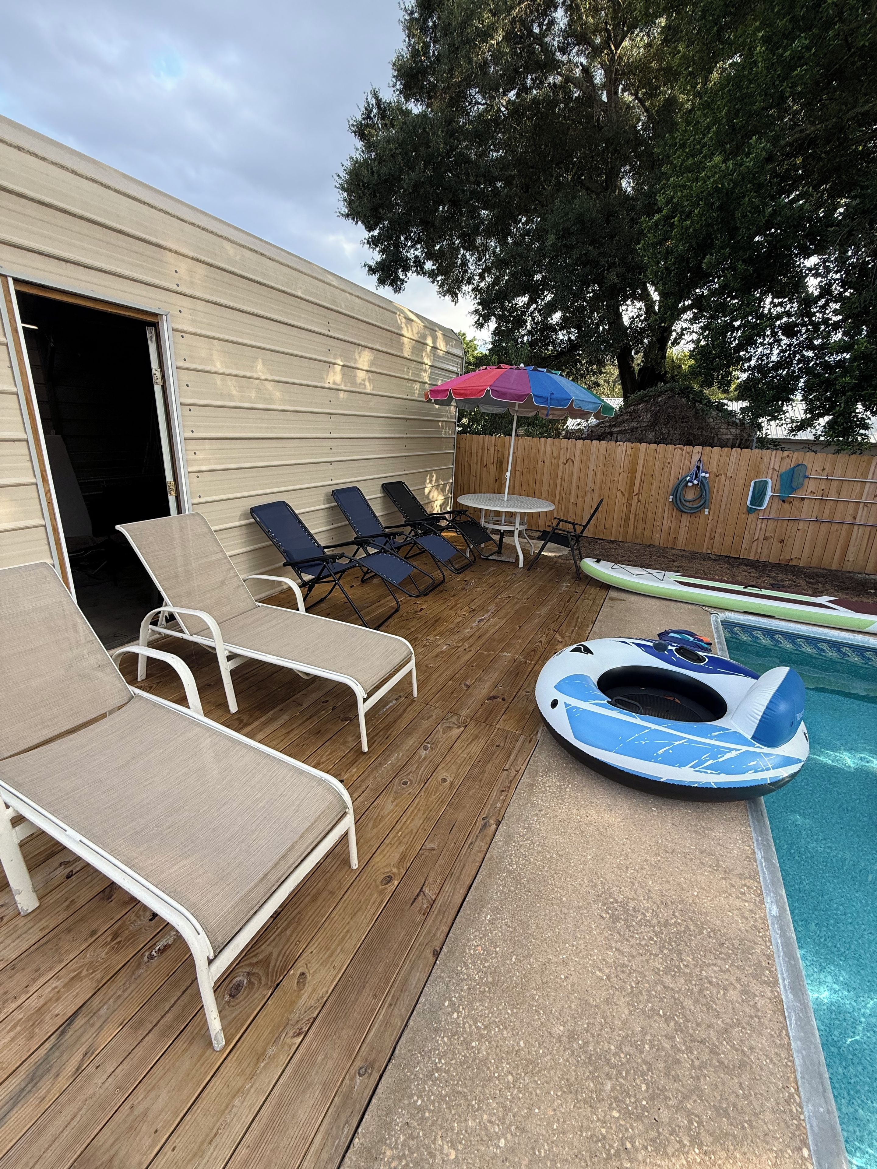 Un área junto a la piscina con sillones de descanso, una mesita y una sombrilla.