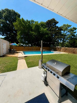 Eine Terrasse im Freien mit Grill, Pool und überdachter Sitzgelegenheit.