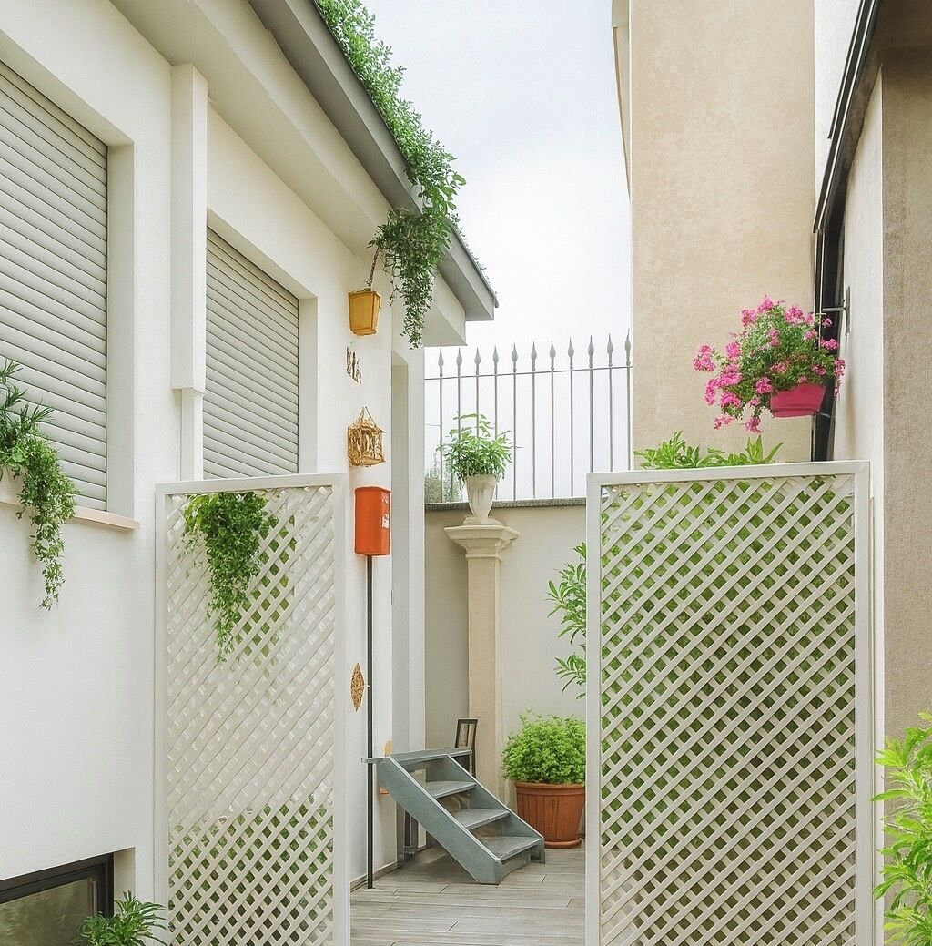 A narrow outdoor space with a white fence, potted plants, a small staircase, and a metal railing.